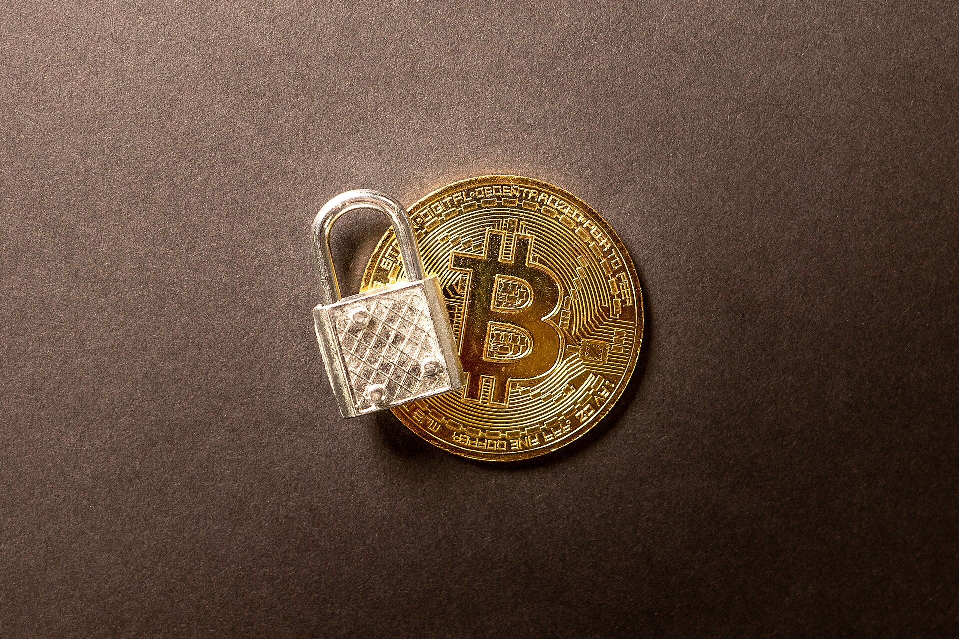 Physical bitcoin token beside a padlock symbolizing cryptocurrency security