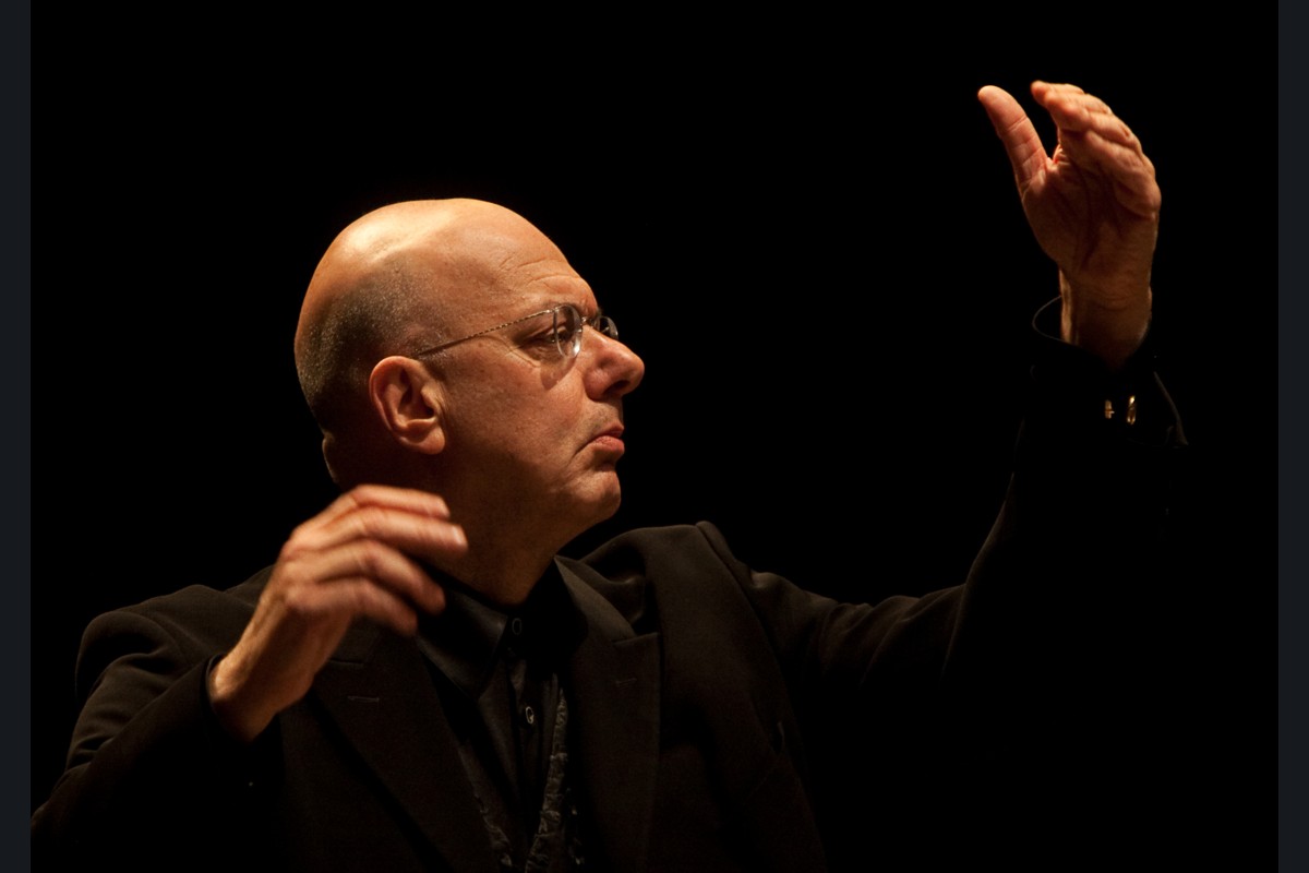 File photograph of Leon Botstein conducting on a dark concert stage, with both arms raised.