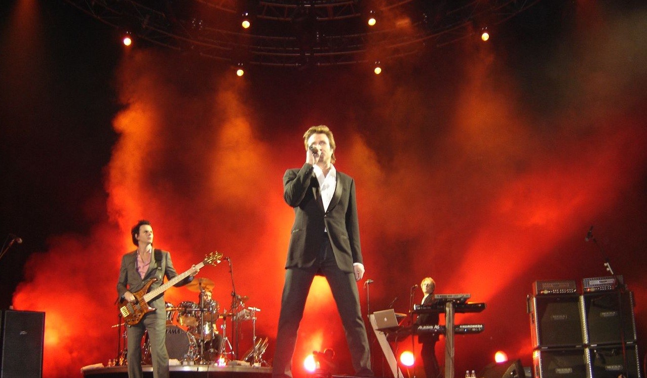 Duran Duran performing on stage under red and orange concert lights