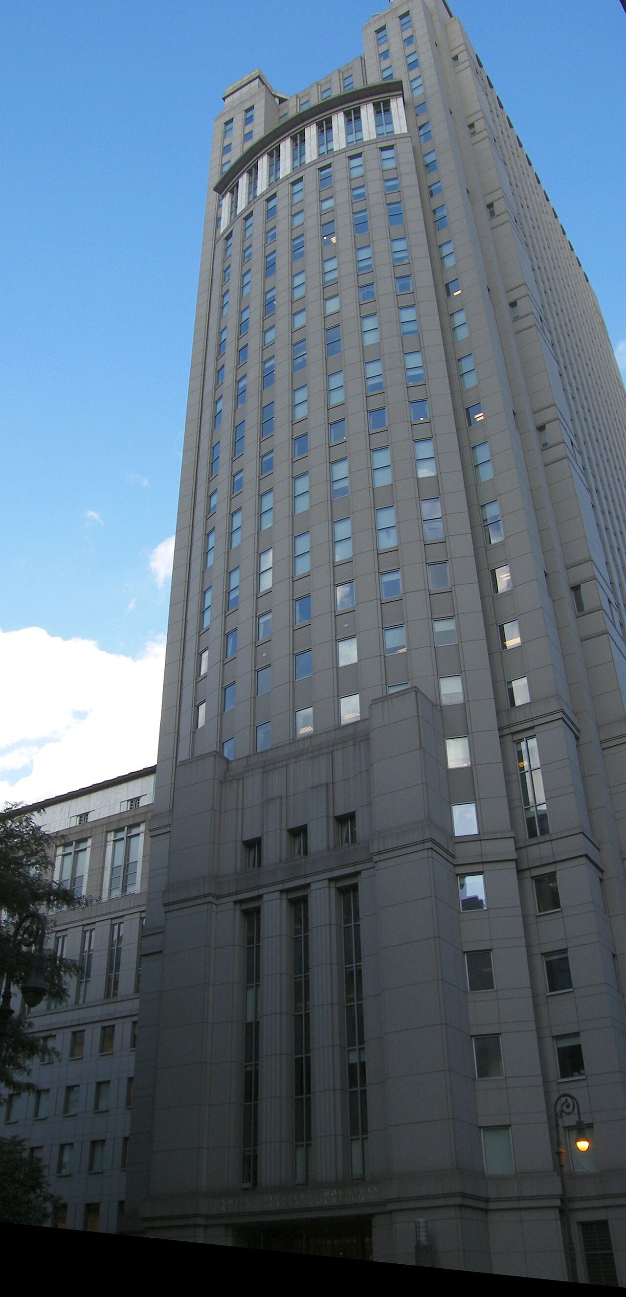 The tall stone and glass facade of the Daniel Patrick Moynihan United States Courthouse in Manhattan under a blue sky