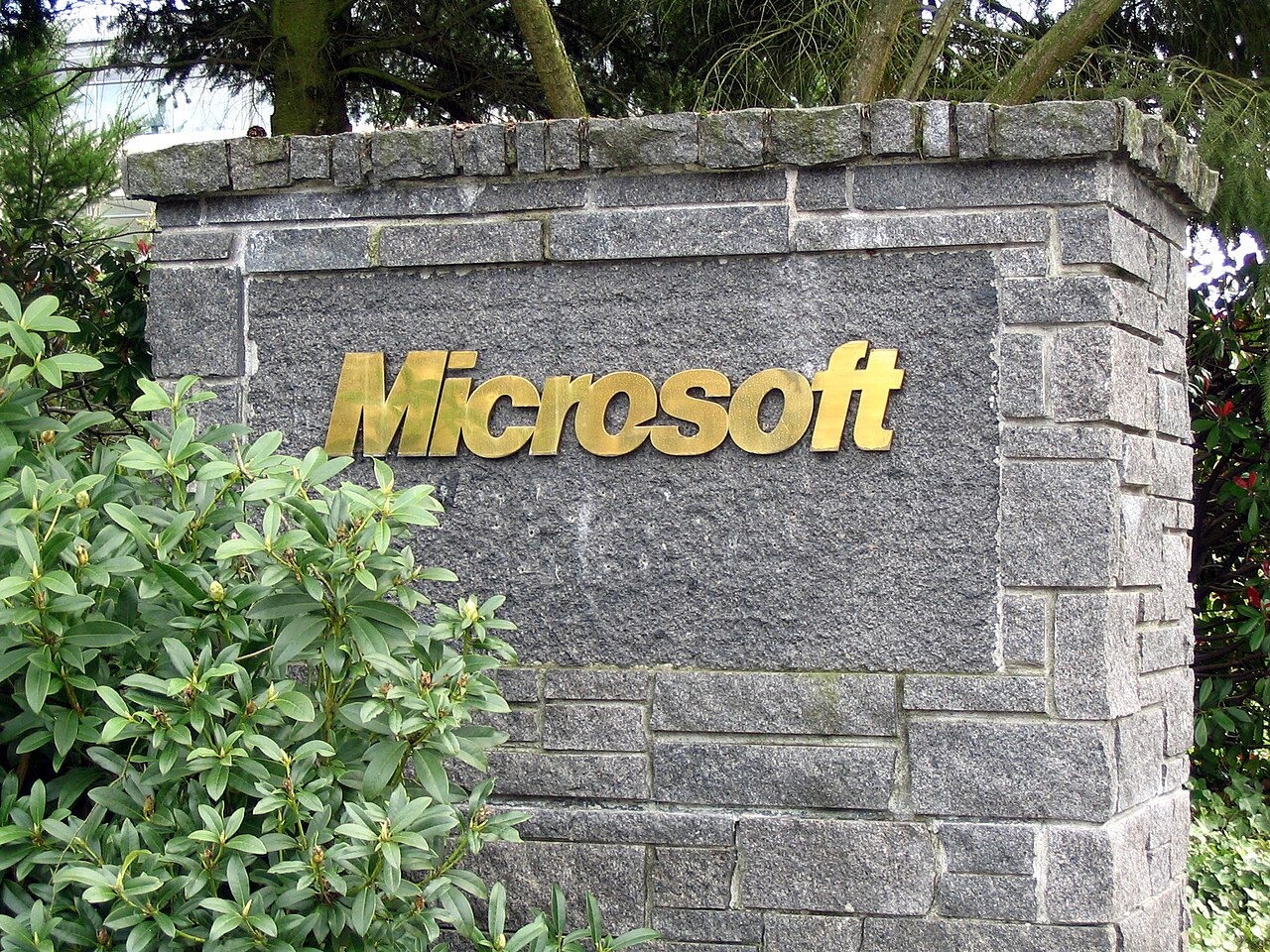 Gold Microsoft lettering on a stone entrance sign surrounded by green plants at the company’s Redmond campus