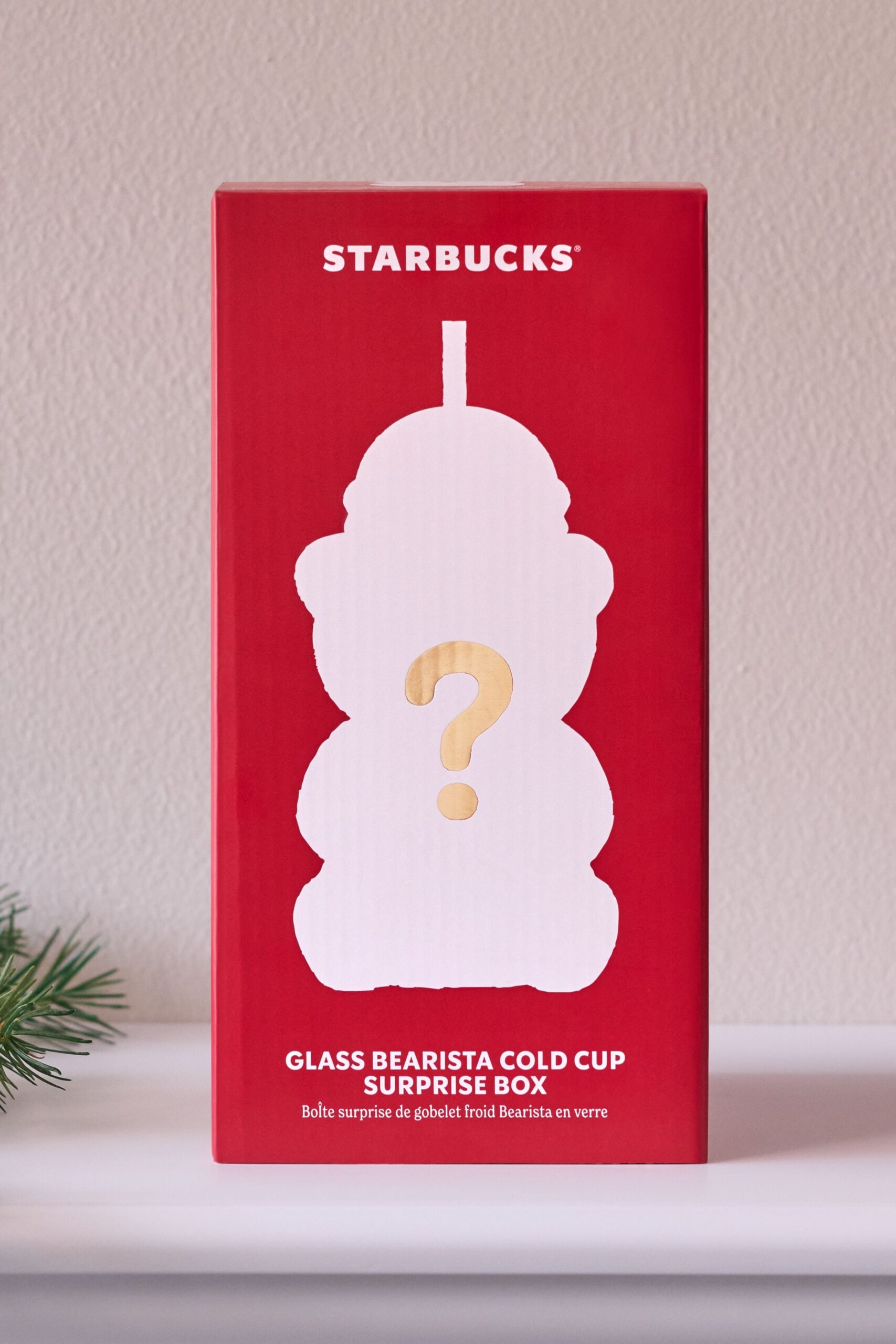 A red Starbucks Glass Bearista Cold Cup Surprise Box with a white bear-shaped silhouette and gold question mark, photographed on a light surface