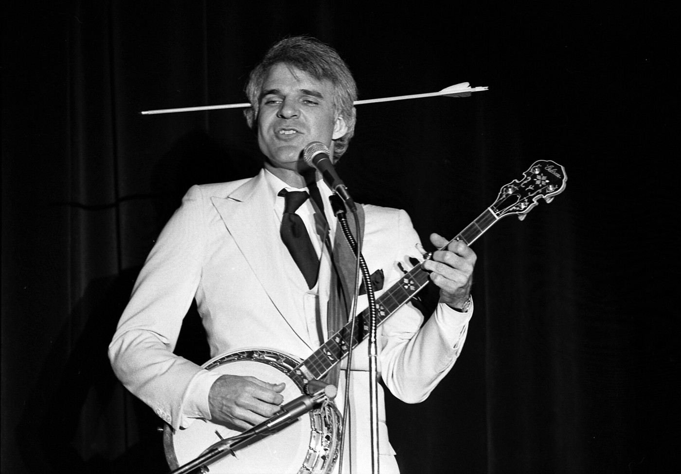 Steve Martin performing with a banjo and his comic arrow-through-the-head prop