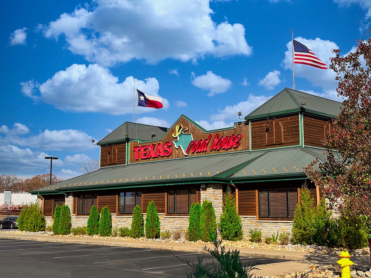 The exterior of a Texas Roadhouse restaurant in California, Maryland, with its red sign, green roof and U.S. and Texas flags.