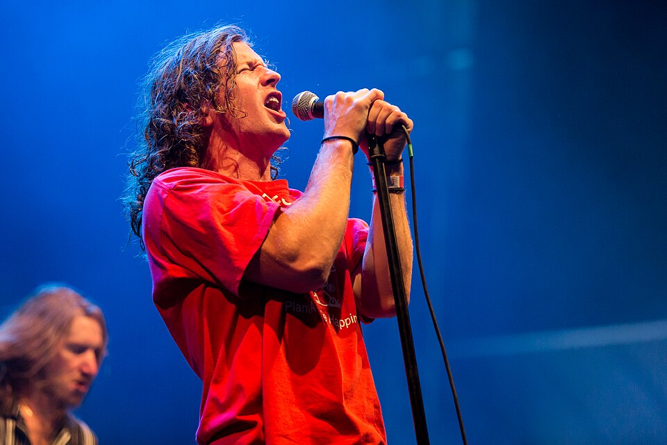 Brendan Yates of Turnstile sings into a microphone wearing a red shirt under blue stage lighting at Full Force festival in 2019.