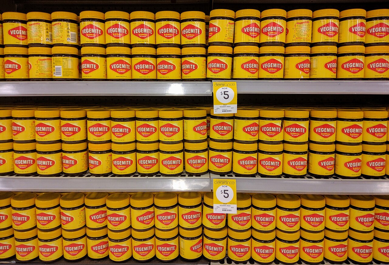 Rows of yellow-lidded Vegemite jars with red and yellow labels on supermarket shelves